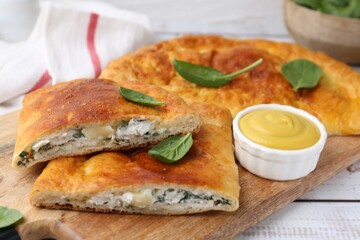 Tasty calzones with basil, cheese and sauce on white wooden table, closeup