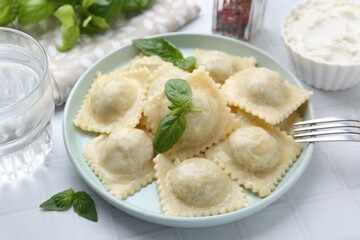 Delicious ravioli with cheese and basil served on white tiled table, closeup