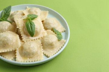 Delicious ravioli with cheese and basil on green background, closeup. Space for text
