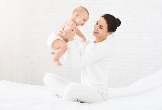 Happy time together. Mother playing with her baby, holding kid on hands in bed