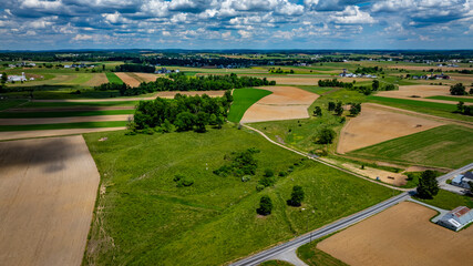 Green and golden fields stretch across the countryside, with a collection of farming buildings in the foreground, set against a clear blue sky.