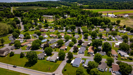 Aerial view of a tranquil rural community featuring various Mobile, Prefab, Manufactured houses situated near lush green fields and trees. The landscape shows harmonious blend of residences farmland.