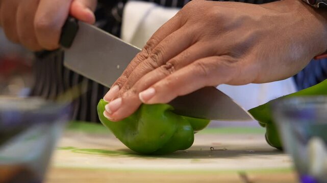 Closeup slow-motion of hands chopping green peppers on a cutting board - food preparation