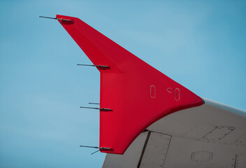 Red arrow-shaped wingtip against clear blue sky. Close-up look of modern airplane detail.