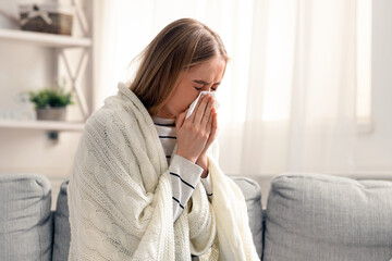 Sick at home. Young woman blowing her nose, empty space