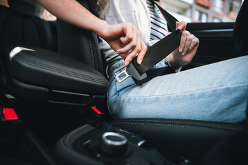 Young woman fastens seatbelt in car, ensuring safety with stylish casual clothing