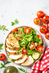 Healthy food. Green salad with grilled chicken meat at white table. Top view.