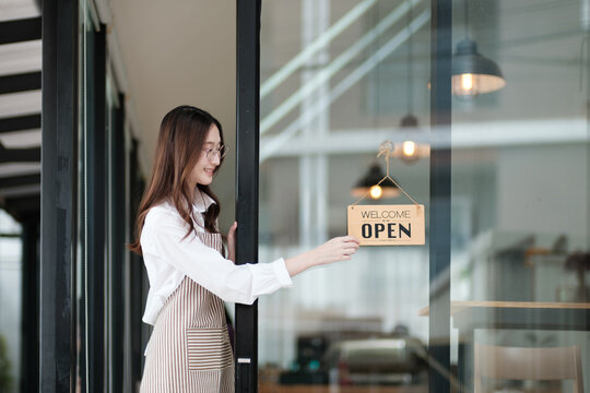 A shopkeeper flipping an open sign at the storefront, letting customers know the shop is now open. The scene highlights the start of a welcoming and professional business day in a retail or cafe.