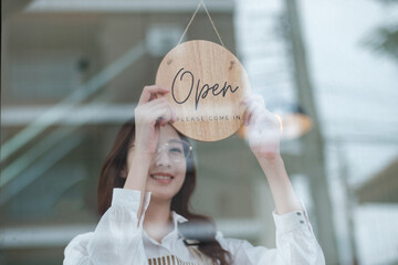 A shopkeeper flipping an open sign at the storefront, letting customers know the shop is now open. The scene highlights the start of a welcoming and professional business day in a retail or cafe.