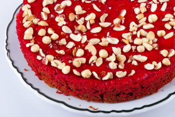 A red cake with nuts and nuts on top. A cake with a red and gray background. Red cake gray background big nuts lies white plate. A large cake with red nuts lies on lifestyle a white plate.