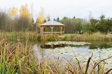 A round gazebo in an autumn park in front of a pond.