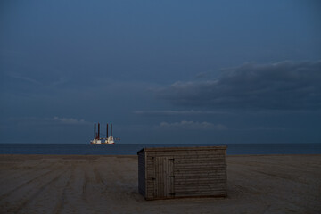 Panoramic view of lonely beach, with dramatic sky and jack up vessel on the horizon.