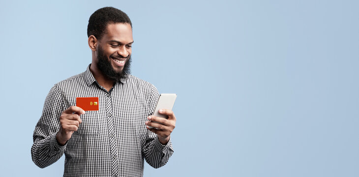 Online Wallet. Smiling blacl man showing credit card, buying via internet isolated over blue studio wall
