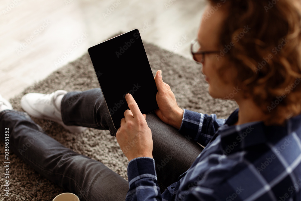 Poster Unrecognizable Man Using Digital Tablet With Blank Screen For Application Or Website Advertisement. Back View Of Guy Browsing Internet On Computer Sitting On Floor At Home. Mockup, High Angle