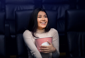 Going to movies alone concept. Lovely Asian woman with popcorn enjoying film in cinema