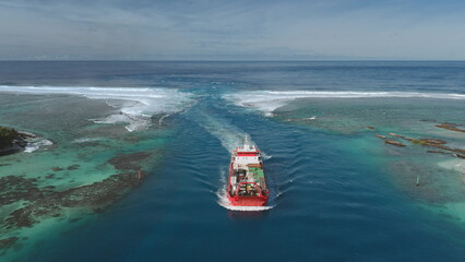 Cargo ship navigating through coral reef passage near Maupiti island in French Polynesia, with...