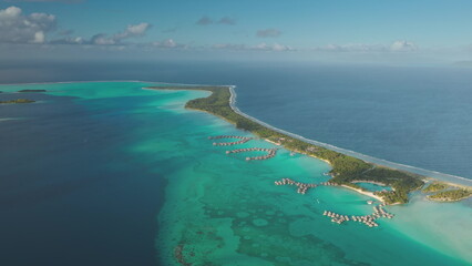 Breathtaking aerial perspective of tropical island coral reef motu, overwater bungalows set in crystal clear turquoise lagoon, vast pacific ocean. Luxury wild nature travel vacation resort. Drone shot
