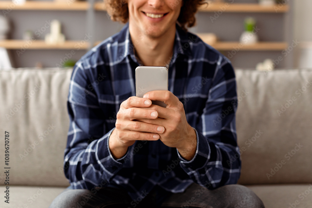 Poster Unrecognizable Hipster Guy Using Mobile Phone Texting And Browsing Internet, Networking In Social Media Online Sitting On Sofa Holding Smartphone At Home. Man With Cellphone Using Application. Cropped
