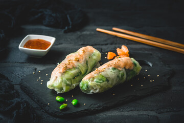 Two summer rolls with salad and salmon on black background, japanese, asian food