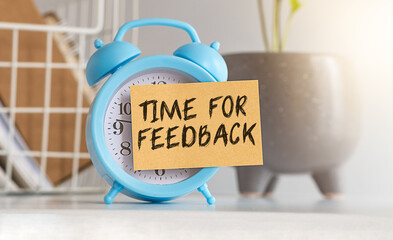 Blue retro alarm clock with a yellow sticky note on a white table with a plant in the background