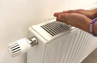Closeup of woman warming her hands on the heater at home during cold winter days, top view. Female getting warm up her arms over radiator. Concept of heating season, cold weather. 