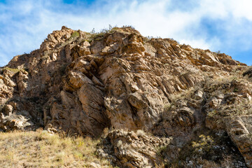 Fototapeta premium A rugged cliffside with exposed rock formations and patches of dry grass under a clear blue sky. A striking natural feature that highlights geological textures and the beauty of untouched landscapes. 