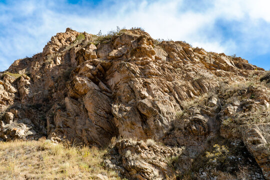 A rugged cliffside with exposed rock formations and patches of dry grass under a clear blue sky. A striking natural feature that highlights geological textures and the beauty of untouched landscapes.
