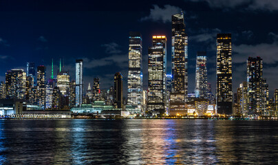 New York City Manhattan midtown skyline at night with lights reflection over Hudson River viewed from New Jersey Weehawken waterfront.