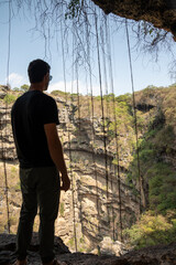 A man stands on the edge of the dramatic Tali Awair sinkhole crater in Oman, gazing into the vast geological formation.