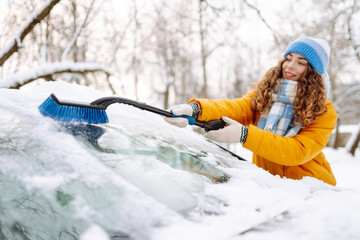 Woman cleaning snow off car during winter snowfall with brush. Scraping ice. Winter cleaning car.