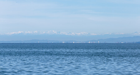 Obraz premium Calm sea with a distant city skyline and snowy mountains under a clear sky. View from the coast of the city of Batumi to the Black Sea and the Caucasus Mountains. The beauty and uniqueness of Georgia.