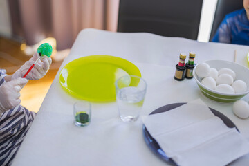 Child paints Easter egg with green paint using brush while sitting at table with paint cups and white eggs. Sweden.