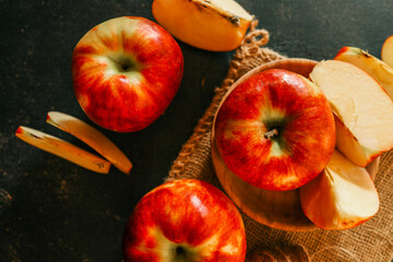 Fresh red apples and apple slices arranged on a rustic burlap cloth with a dark textured background, creating a cozy, autumnal food composition