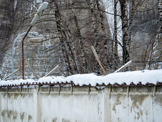 close-up of a wall with barbed wire behind which is a closed area. Winter. snow