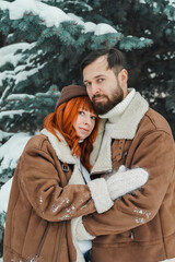 Love romantic couple lovestory. Brutal bearded man, bright red-haired girl woman in winter park. Romantic date, kissing, hugging. Walking, having fun. Stylish clothes, red sheepskin coat, jacket, hat