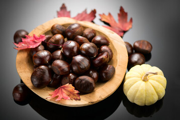 Fototapeta premium Chestnut, Fresh sweet chestnuts with autumn red leaves and little decorative pumpkin on black background, top view. Thanksgiving day. Edible chestnuts (Castanea sativa) in wooden bowl.