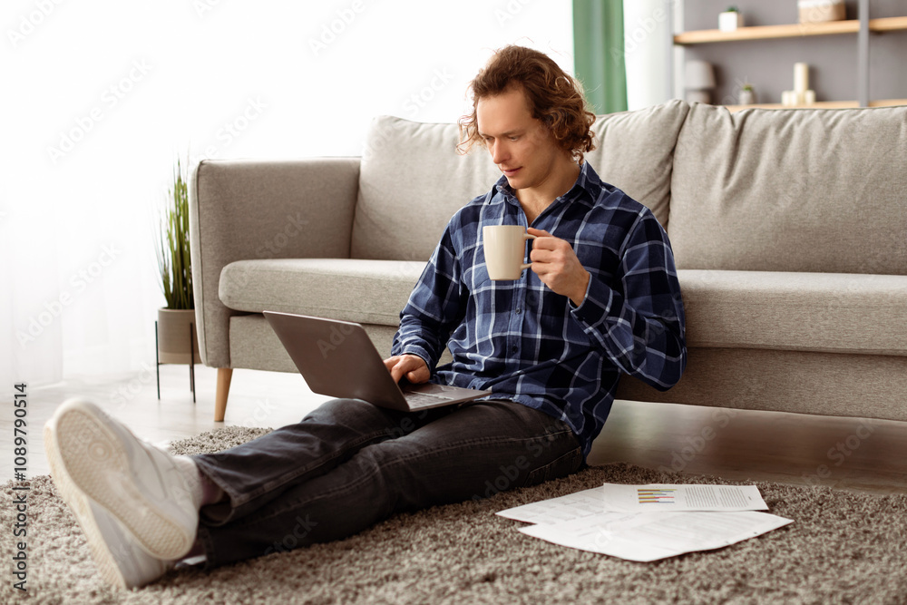 Poster freelance work. serious guy using laptop computer working online and drinking coffee sitting on floo