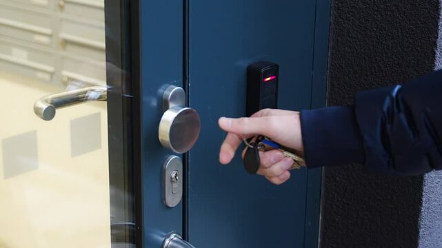Close up view of person using a electric lock key fob to access a building via a reader of entry system mounted on a house wall