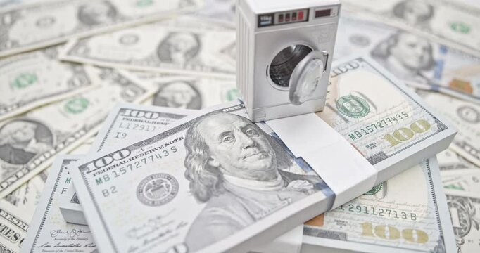 Money laundering, financial crimes, corruption, legal enforcement and economic justice : A miniature washing machine on a stack of US dollar 100 bills, symbolizing the concept of "money laundering".