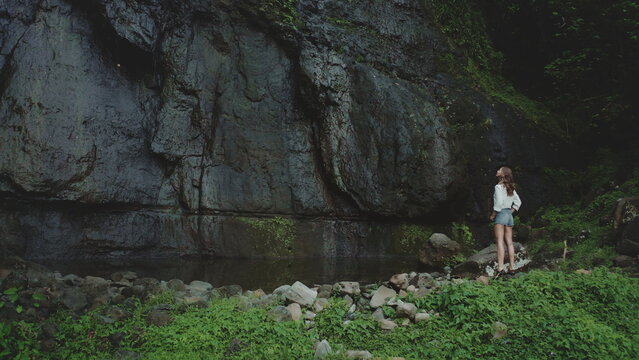 Young woman is enjoying the tranquility of nature, standing in awe of a magnificent waterfall crashing down a sheer rock face