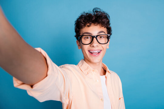 Cheerful young man with curly hair and braces smiling on a blue background