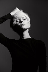 Stylish woman with short blonde hair posing dramatically against a dark background. Elegant fashion...