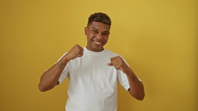 Young man expressing excitement and joy in white shirt against isolated yellow wall background