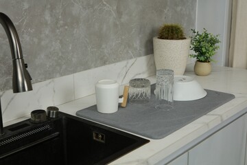 dish drying mat is placed on a kitchen countertop next to a sink. A variety of clean dishes,...