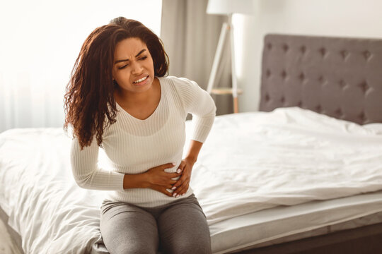 People, Healthcare and Health Problem Concept. Portrait of upset sick young black woman suffering from acute pain in right side, sitting on bed at home, free copy space. Abdomen liver pain