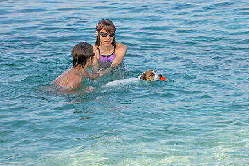 children playing ball in the clear sea with a jack russell terrier. Traveling with pets. School holidays