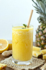 Pineapple ginger lemon smoothie in glass with bamboo straw on wooden table with white background....