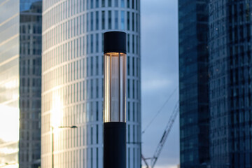 Obraz premium Modern lighting lamp illuminates the city, with office buildings in the background. The scene represents concepts such as electricity prices, power supply, and urban infrastructure.