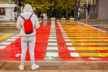 Person wearing a white puffer jacket and red backpack standing at a bright crosswalk on a rainy day