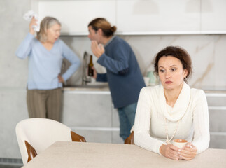 Obraz premium In kitchen, man is quarreling with elderly mother, during quarrel, sad woman is present and listens to this
